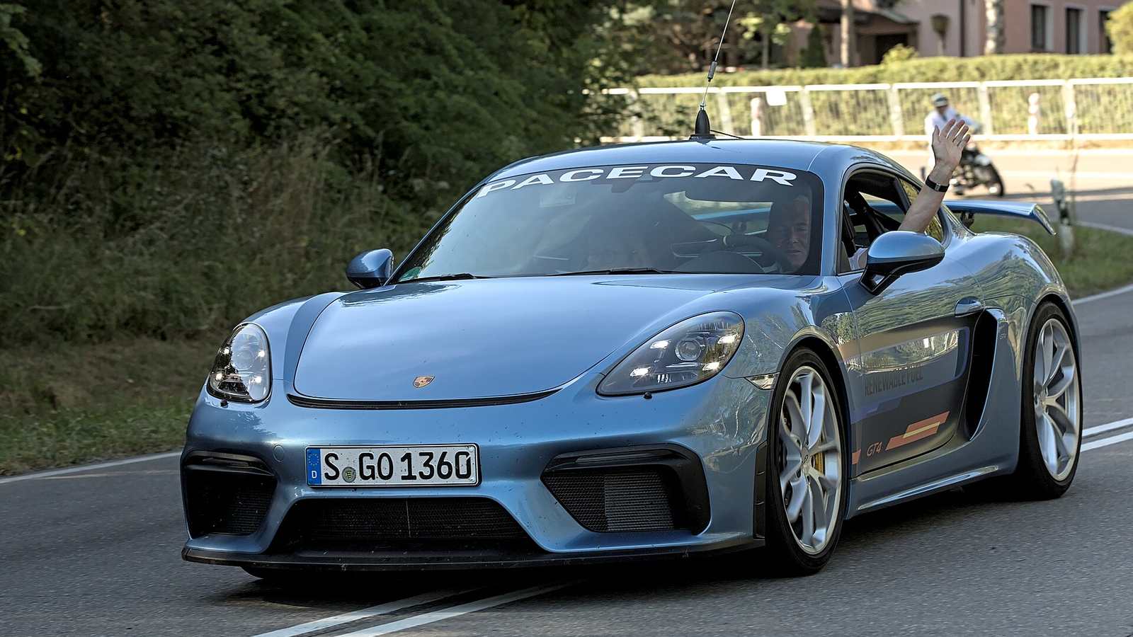 A blue-grey Porsche 718 Cayman GT4 on a public road at a historic motorsport event