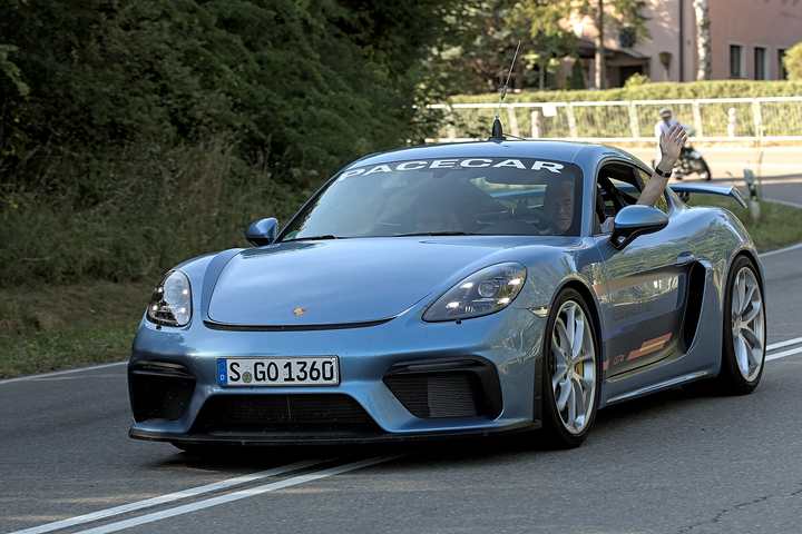 A blue-grey Porsche 718 Cayman GT4 on a public road at a historic motorsport event