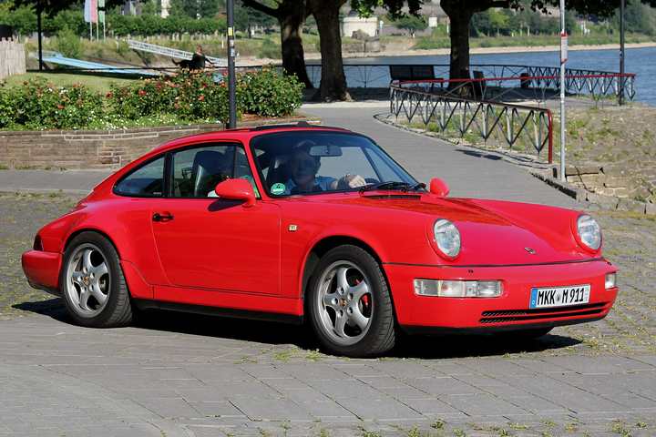 A red Porsche 911 Carrera of the 964 generation parked beside a river promenade