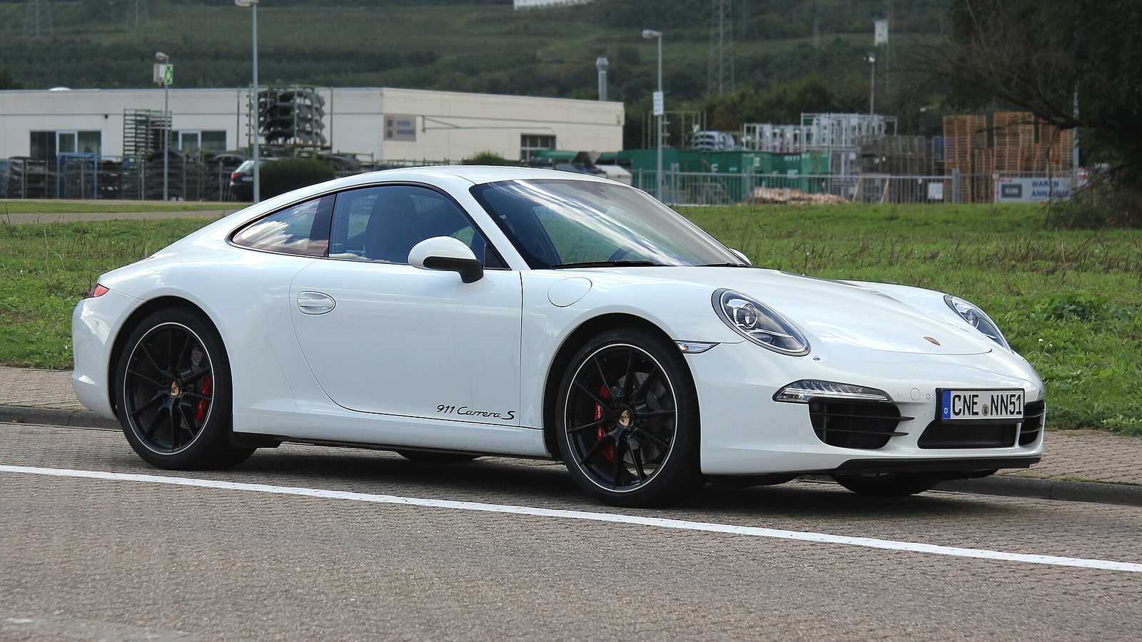 A white Porsche 911 Carrera S of the 991 generation driving past a field
