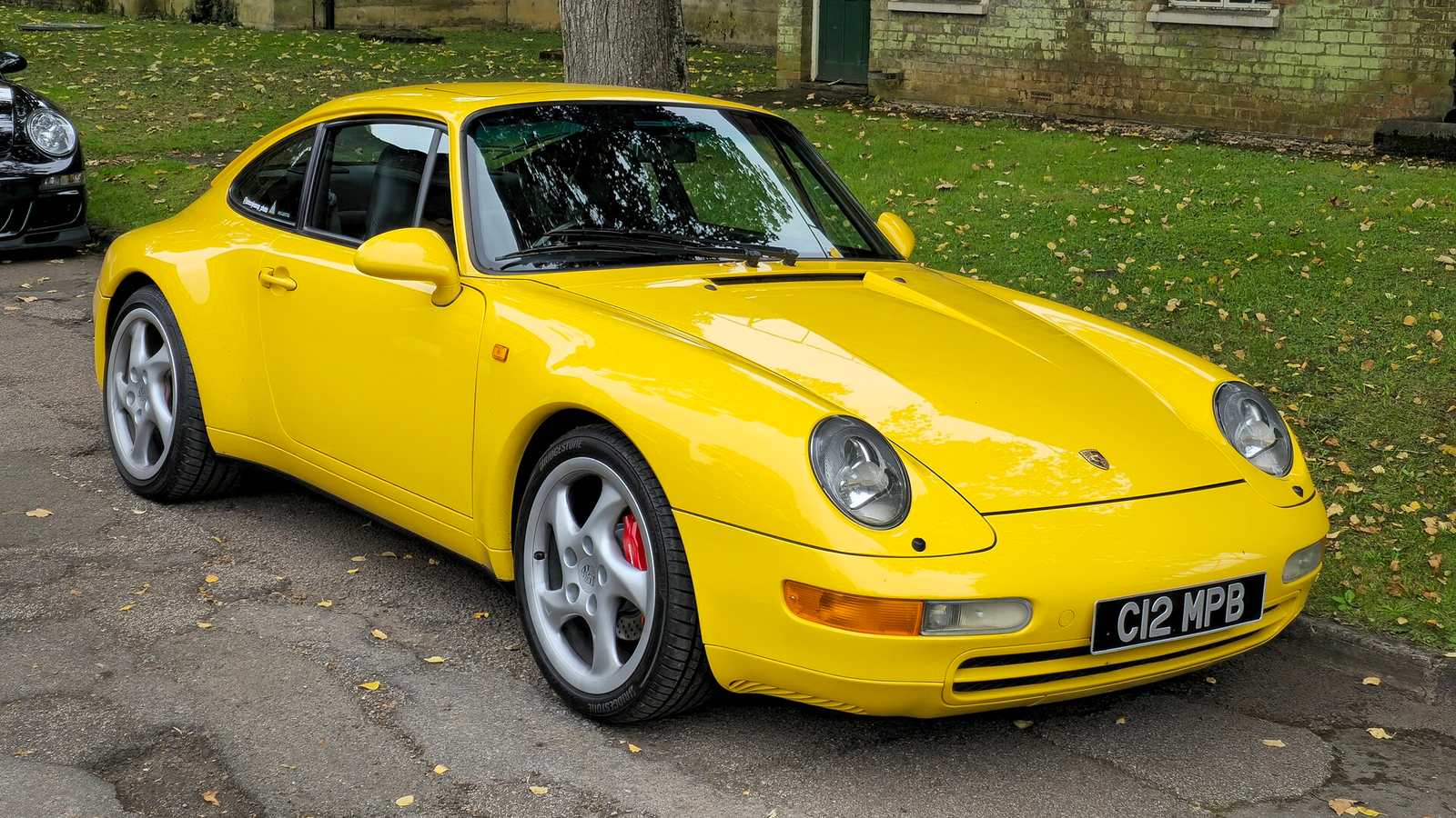 A yellow Porsche 911 Carrera of the 993 generation parked on a tree-lined street