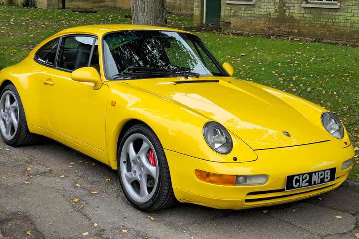 A yellow Porsche 911 Carrera of the 993 generation parked on a tree-lined street