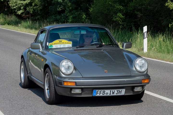 A grey impact-bumper Porsche 911 coupé on a country road during a classic rally