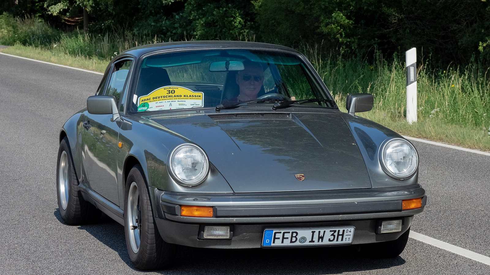 A grey impact-bumper Porsche 911 coupé on a country road during a classic rally