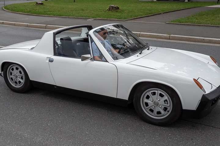 A white Porsche 914 with its roof panel removed driving through a town