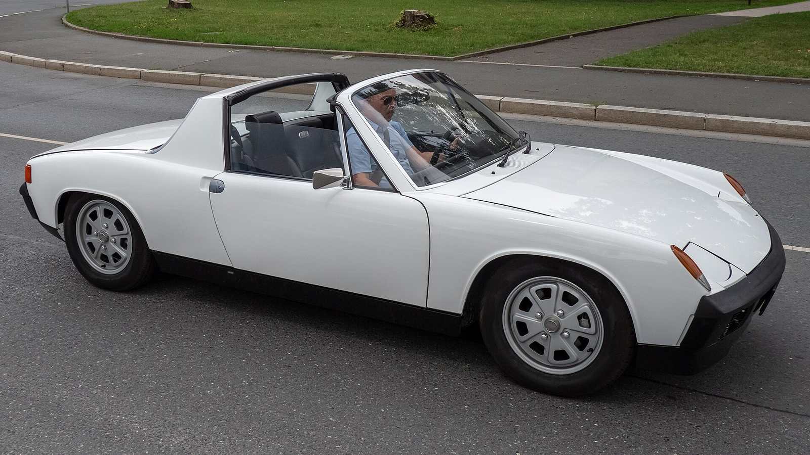 A white Porsche 914 with its roof panel removed driving through a town
