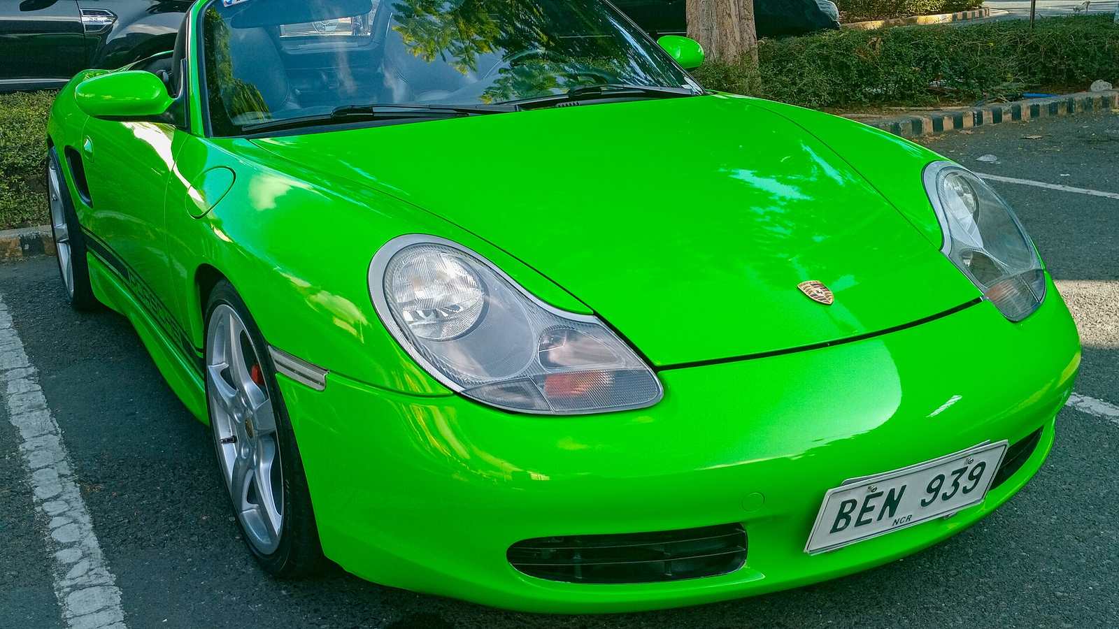 A bright green Porsche Boxster of the 986 generation parked in a car park