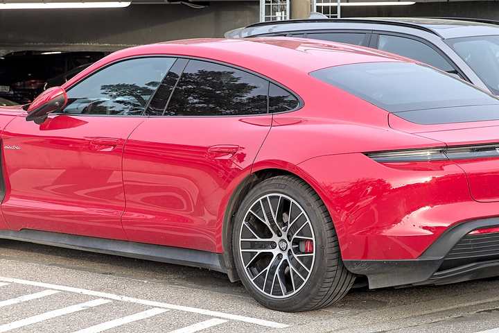 A red Porsche Taycan 4S parked in a car park, seen from the rear three-quarter