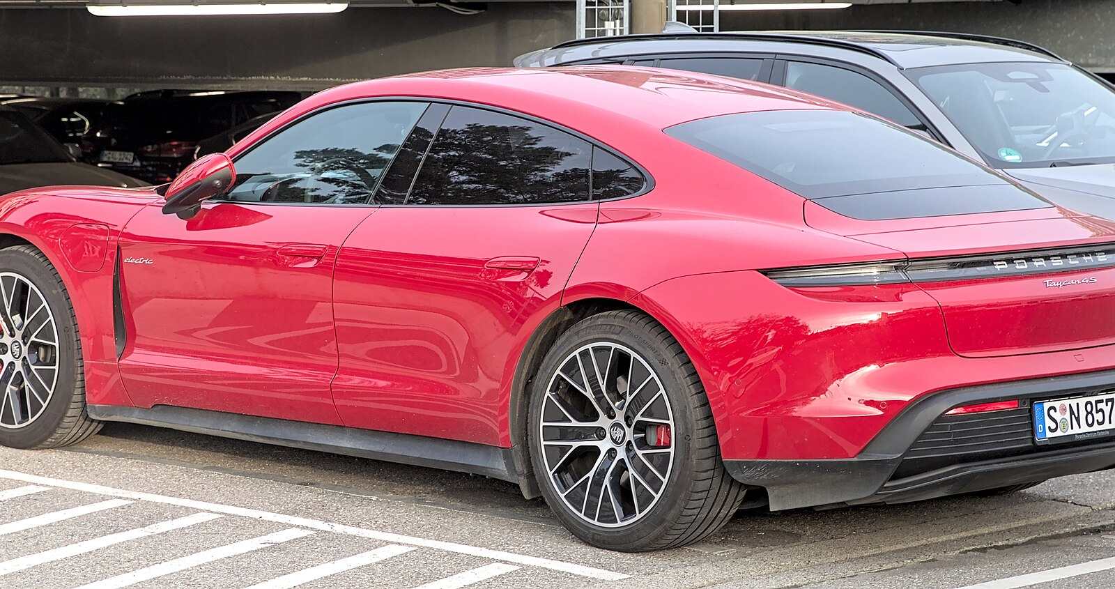 A red Porsche Taycan 4S parked in a car park, seen from the rear three-quarter